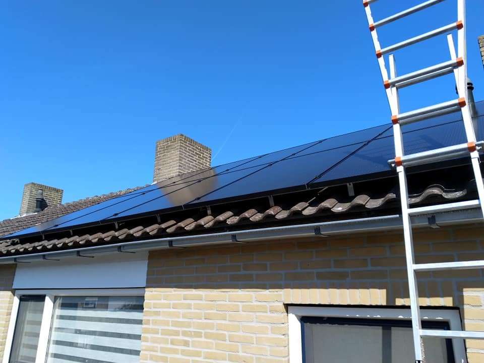 Zwarte zonnepanelen op het dak van een bungalow met ladder ernaast